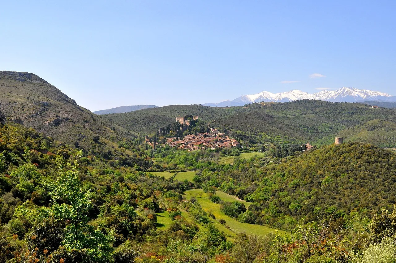 Pueblo del Pirineo en un valle verde, con la sierra nevada al fondo